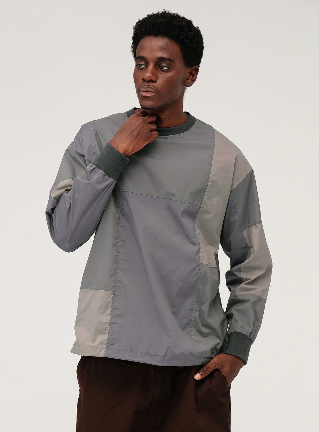 Model wearing a gray and beige patchwork long-sleeve shirt with an adjustable hem.