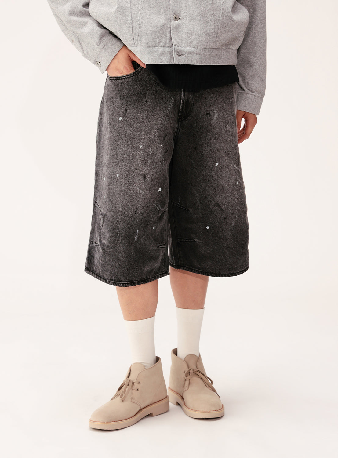A person wears BEAMS Quarter-Length Painter Denim Pants, a grey jacket, white socks, and beige desert boots, standing with hands in pockets against a plain light background. The image is cropped at the chest.