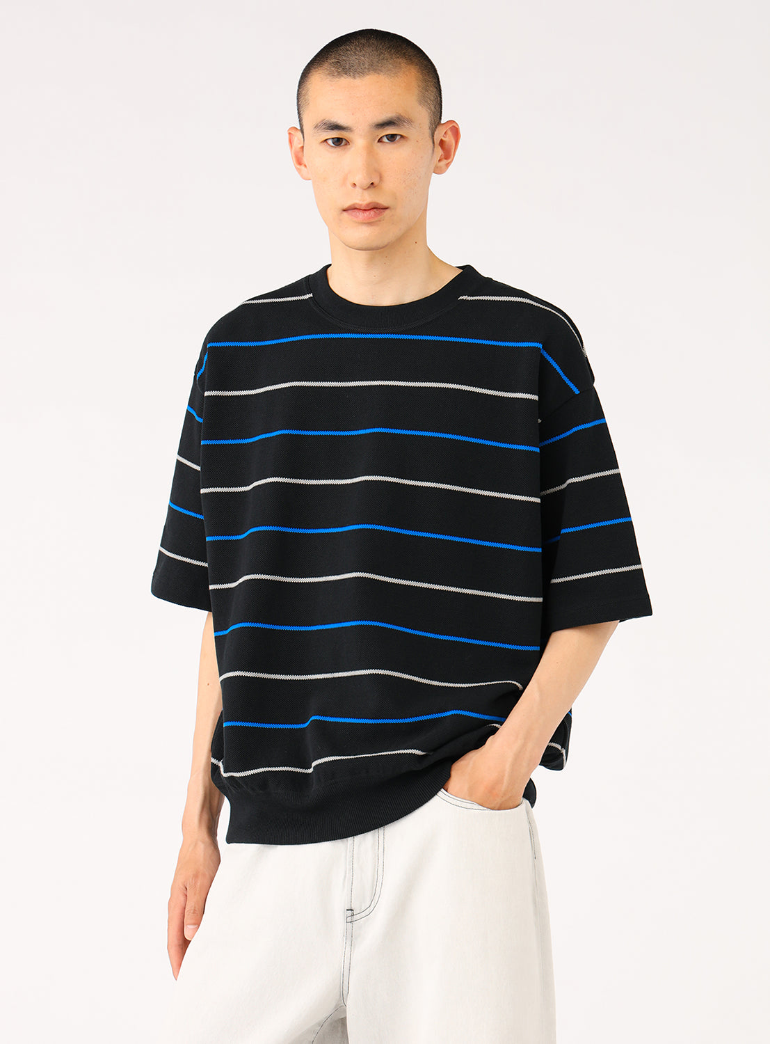 Model wearing a black knit shirt with blue and white stripes and light pants, front view, displaying relaxed fit.