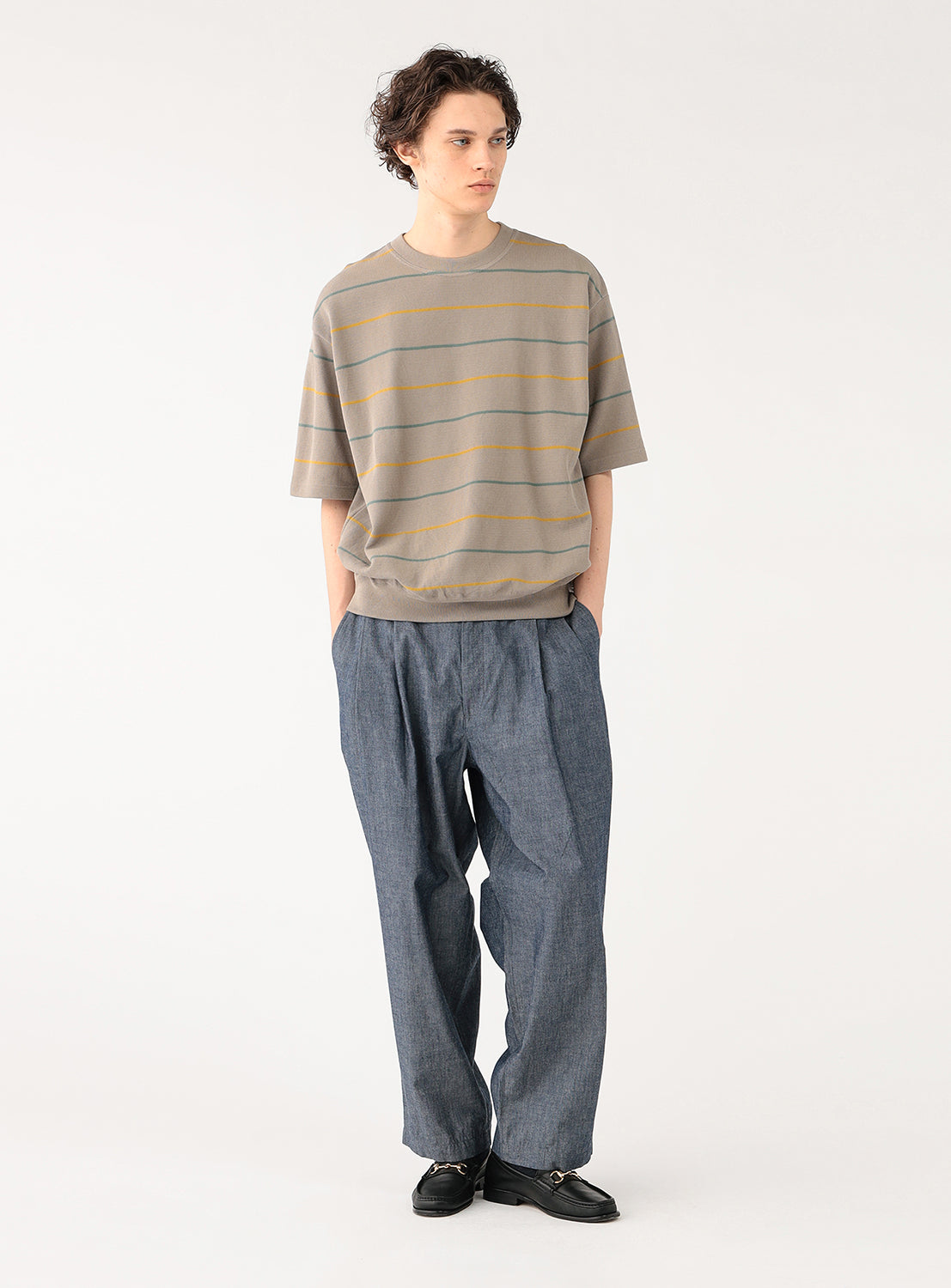 Model wearing a taupe striped knit shirt and blue pants, front view, displaying its relaxed fit.