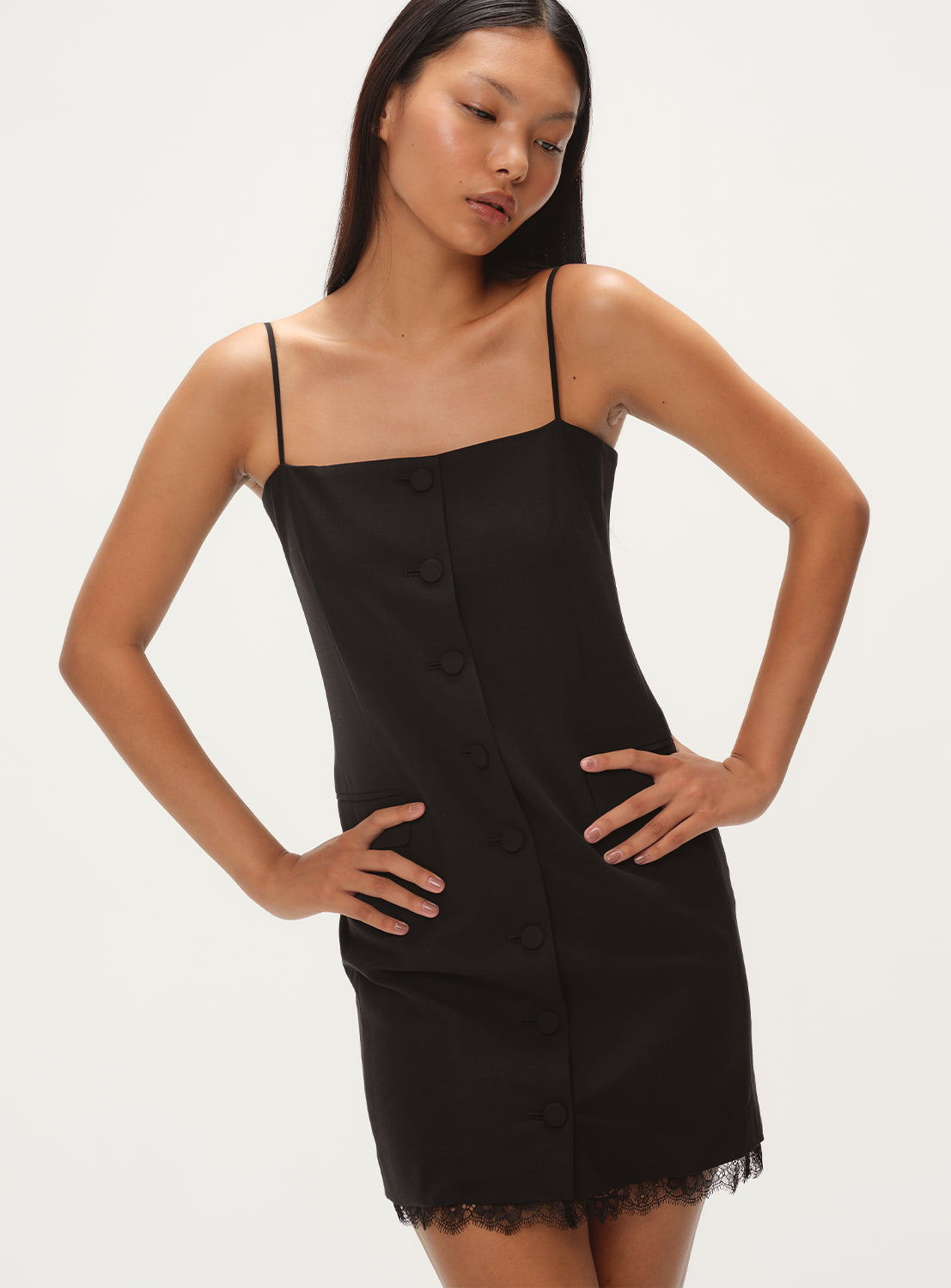 Model wearing a black mini dress with thin straps, button down the front, and a lace hem at the bottom.