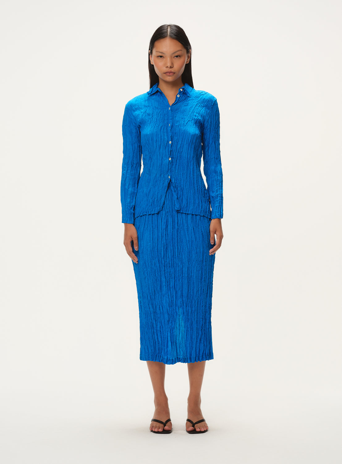 Full body shot of a model wearing a matching blue crinkled top and pleated midi skirt set.