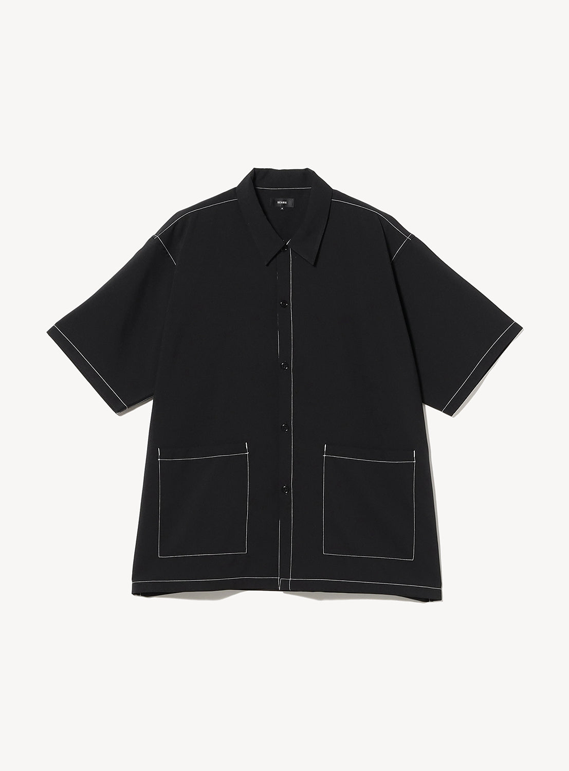The BEAMS Wide Fit Double Pocket Contrast Stitch Shirt is a short-sleeved, black utility button-up featuring two large front pockets and striking white contrast stitching along the seams, pockets, and edges. Made from moisture-wicking performance fabric, it is shown against a plain white background.