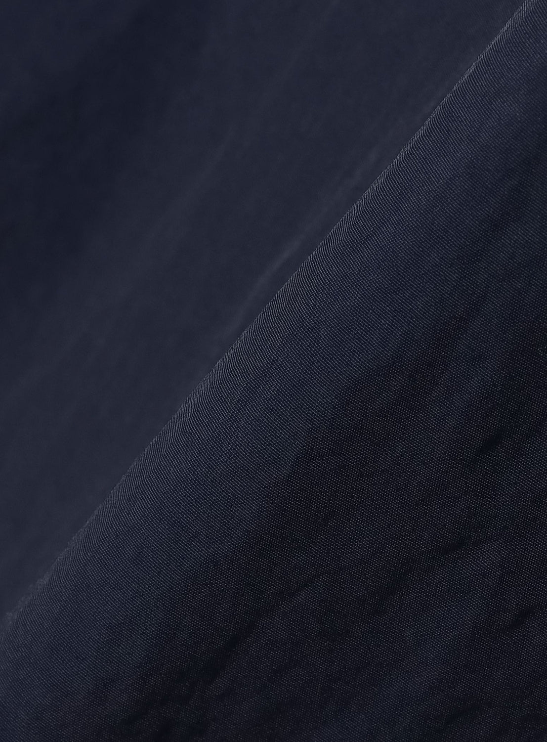 Close-up of dark navy blue fabric with a soft texture, shown at an angle. Fine lines and subtle shading highlight the material’s smooth and slightly shiny finish—evoking vintage training wear in the BEAMS T Tyrrell Winston - Anorak Jacket collaboration featuring the signature WIN SPORT logo.