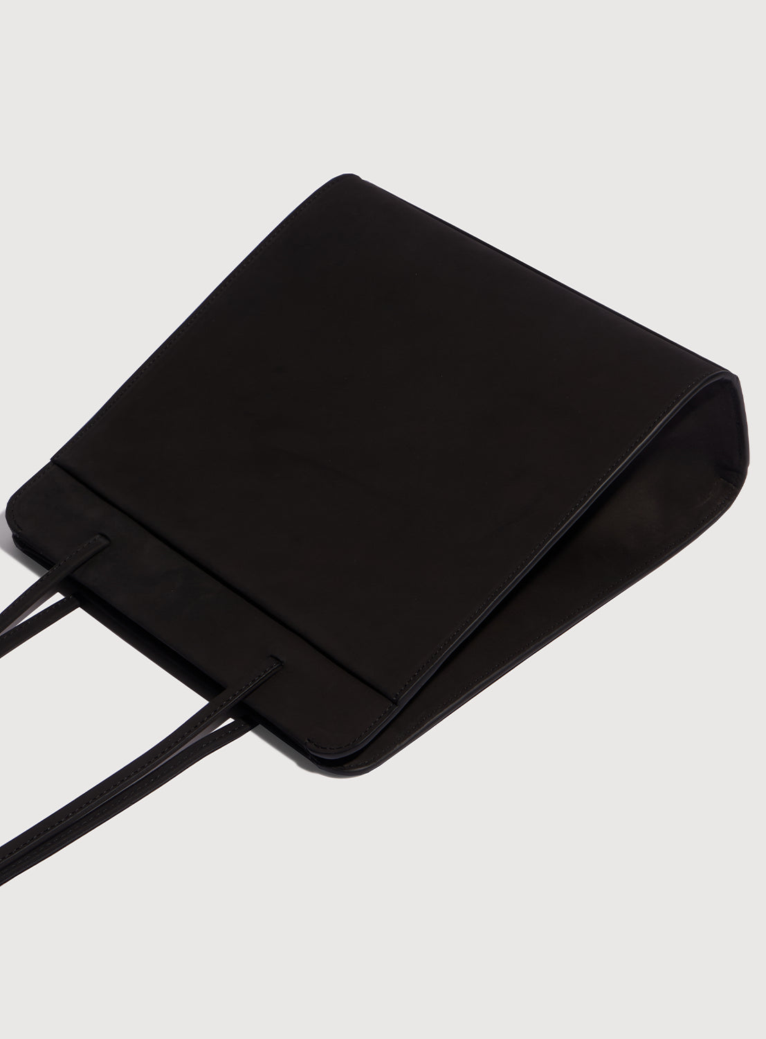 Black square handbag with long, ribbon-like straps, featuring the side shape.