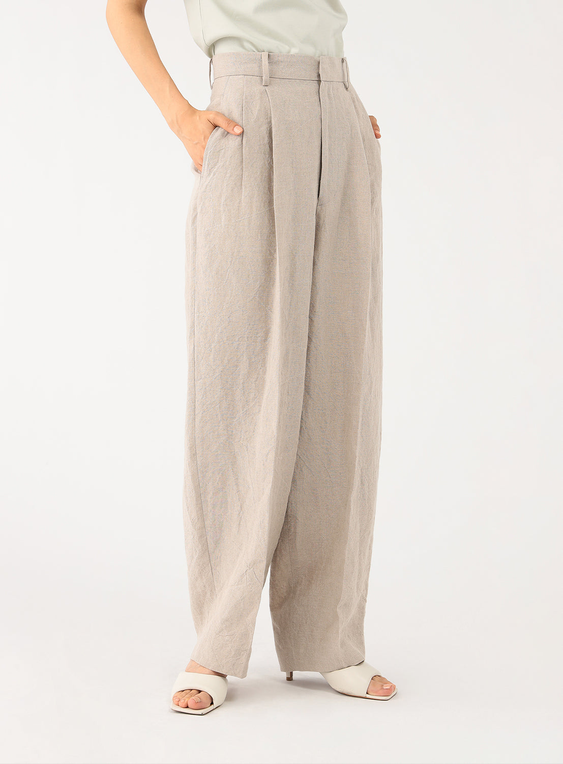 Side view of a model wearing off-white pleated pants, styled with a light t-shirt and white sandals.