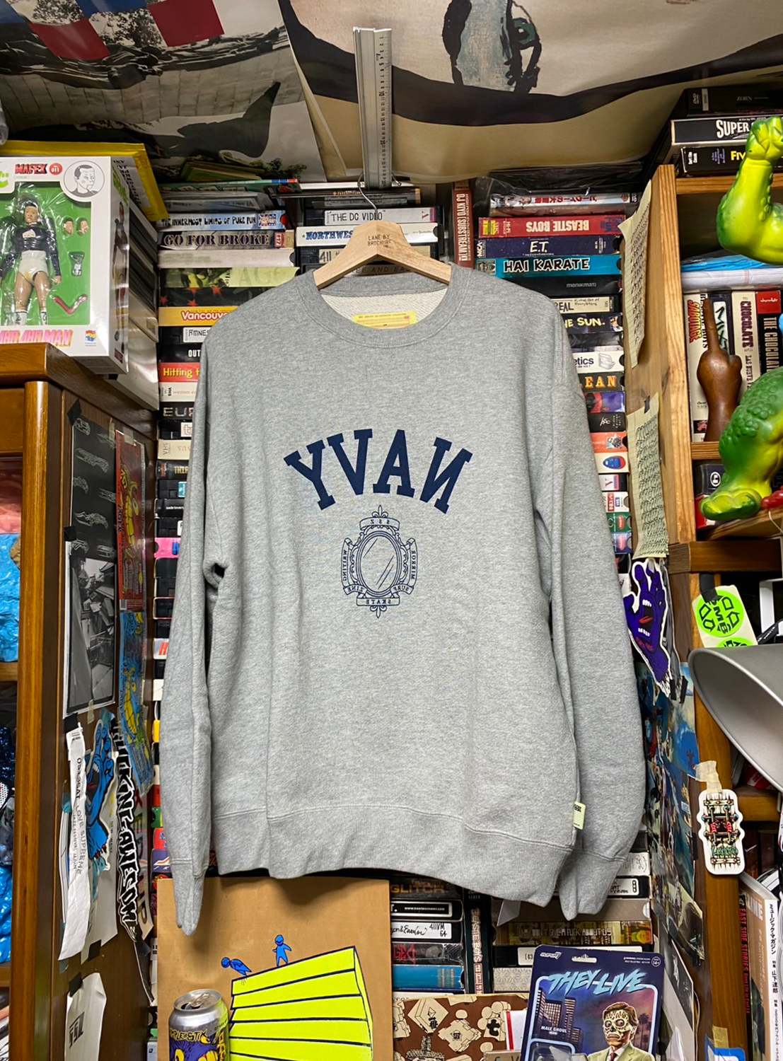 A gray sweatshirt with the text 'YVAN' and a graphic on the front, displayed on a hanger among various items.