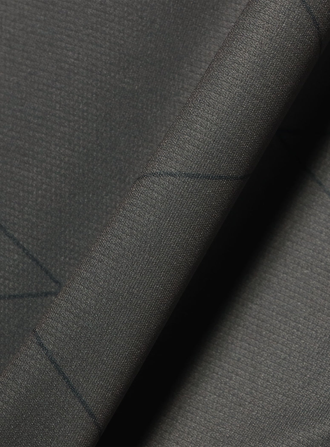 Close-up of dark gray, moisture-wicking polyester fabric with a subtle grid texture and faint diagonal lines, showing a folded edge—part of the BAL × UMBRO Soccer Jersey, a BAL collaboration inspired by retro football design.