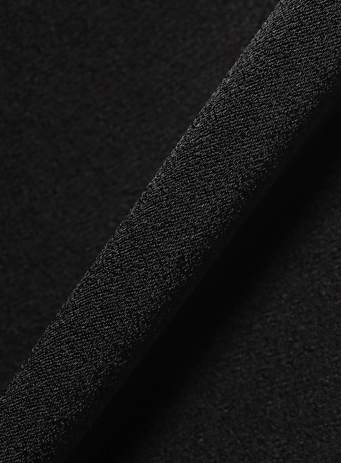 Close-up view of the KANAKO SAKAI Satin Cargo Trousers in black, showcasing their textured surface with a thick, diagonal strip running from the bottom left to the top right. Both areas feature a slightly rough, grainy feel and subtle sheen reminiscent of satin fabric, highlighting the trousers' distinctive tactile texture.