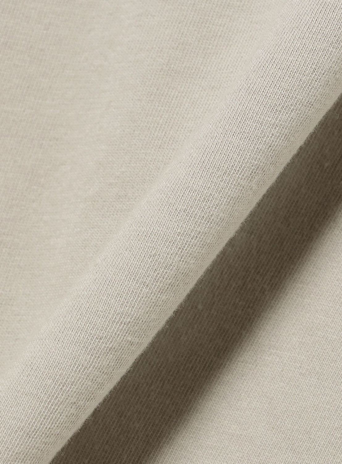Close-up of beige fabric with a visible weave texture, folded diagonally across the image, highlighting the soft and subtly textured surface—ideal for a relaxed fit BAL IG The Prophet graphic T-shirt.