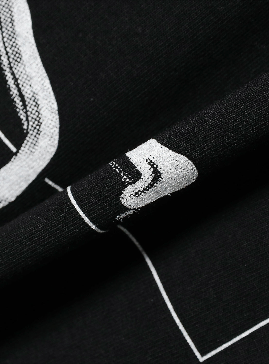 Close-up of black t-shirt fabric, detailing the white graphic print of an abstract shape and textile texture.
