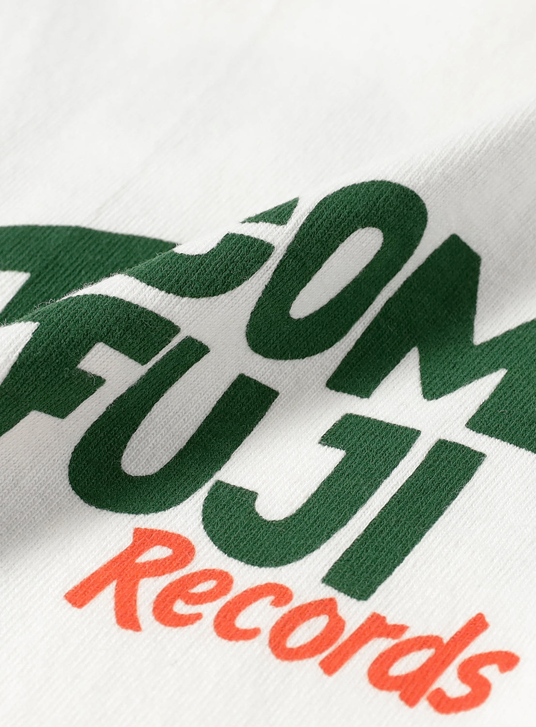 Close-up of white t-shirt fabric, detailing the green "TACOMA FUJI" and orange "Records" graphic print.
