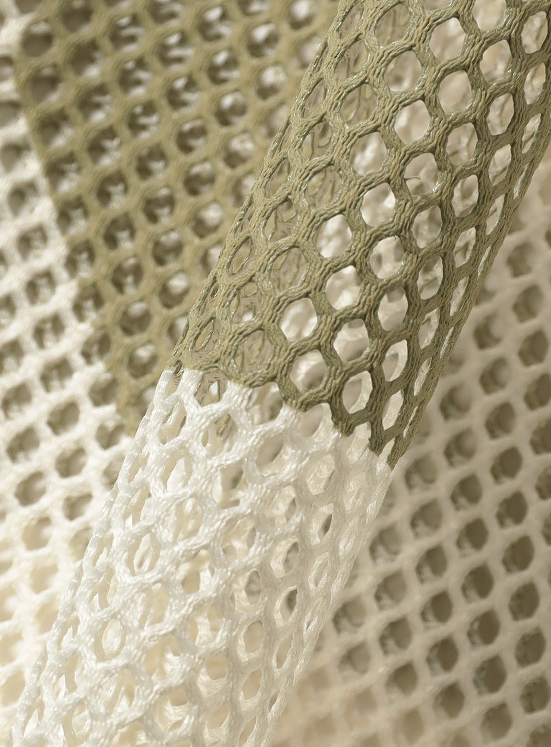 Close-up of cream mesh jersey fabric, detailing the porous texture and contrasting grey stripe.
