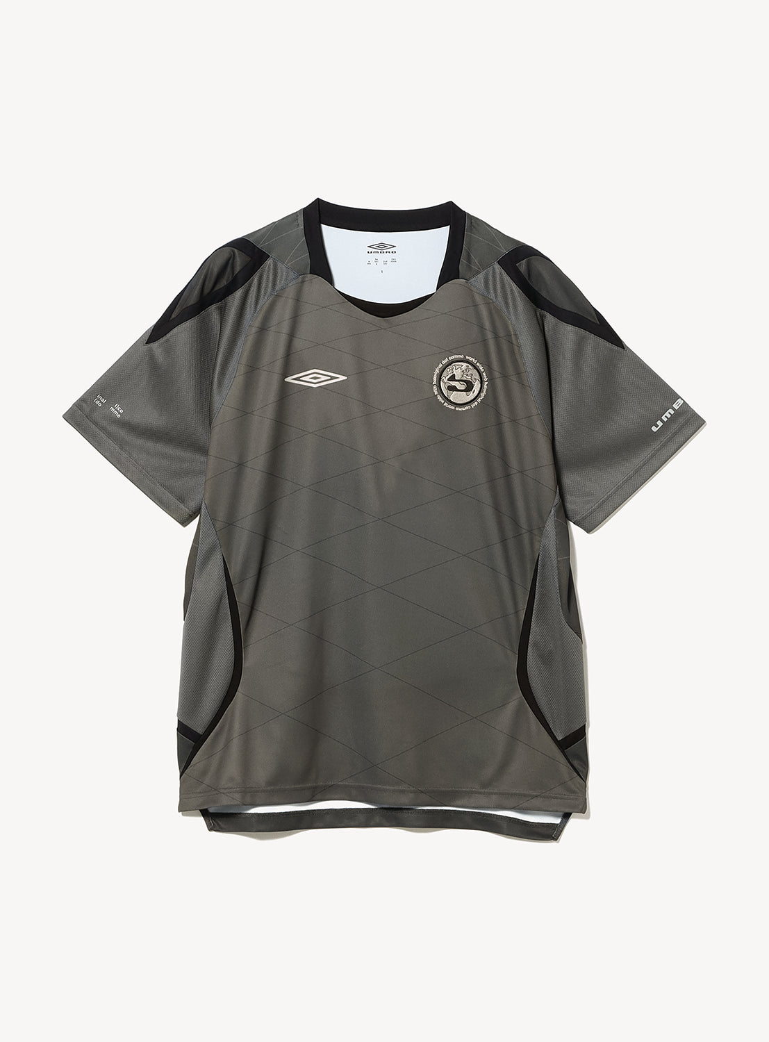 The BAL × UMBRO Soccer Jersey by BAL is a gray and black short-sleeve jersey featuring geometric patterns and a retro football-inspired design. It showcases the UMBRO logo alongside a circular team crest on the chest and is crafted from moisture-wicking polyester, presented here against a white background.