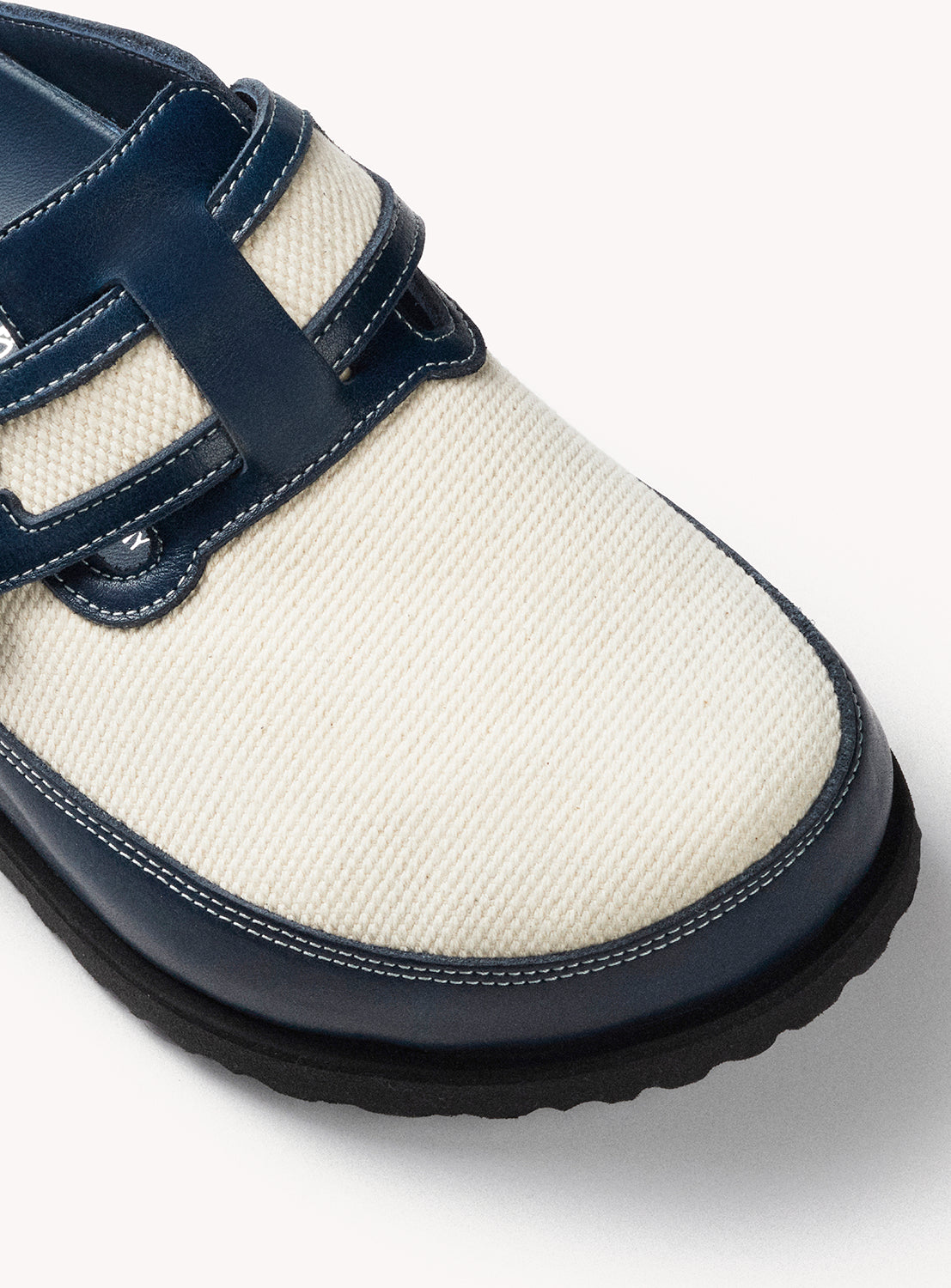 White shoe with navy blue straps on a light gray background