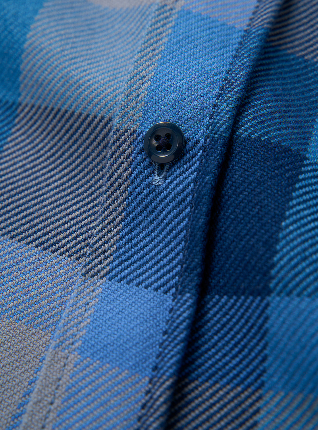 Close-up of the BEAMS Indigo Check Shirt, featuring blue and gray plaid fabric with a single black button sewn on—highlighting the texture and classic pattern that make this relaxed-fit shirt a timeless staple.