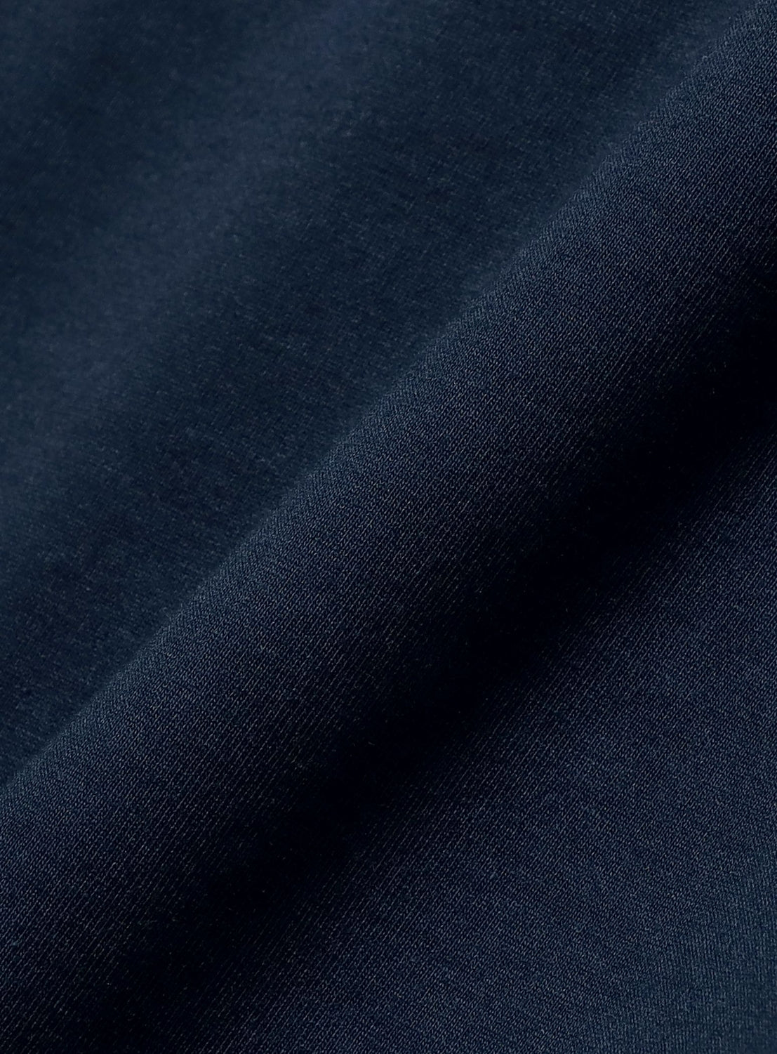A close-up of dark blue fabric with a smooth texture and a visible diagonal seam or fold evokes the minimalist design of the BEAMS Signature Logo Basic Fit T-Shirt, subtly featuring the brand's logo often found on classic crew neck styles.