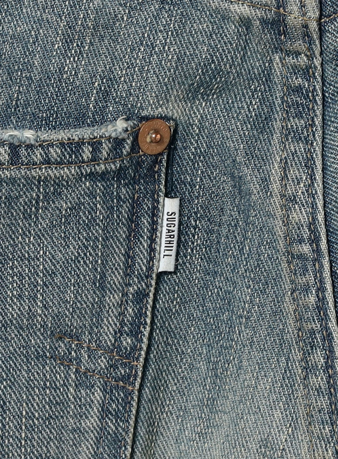 Close-up of a blue denim pocket with a button and 'SUGARHILL' label.