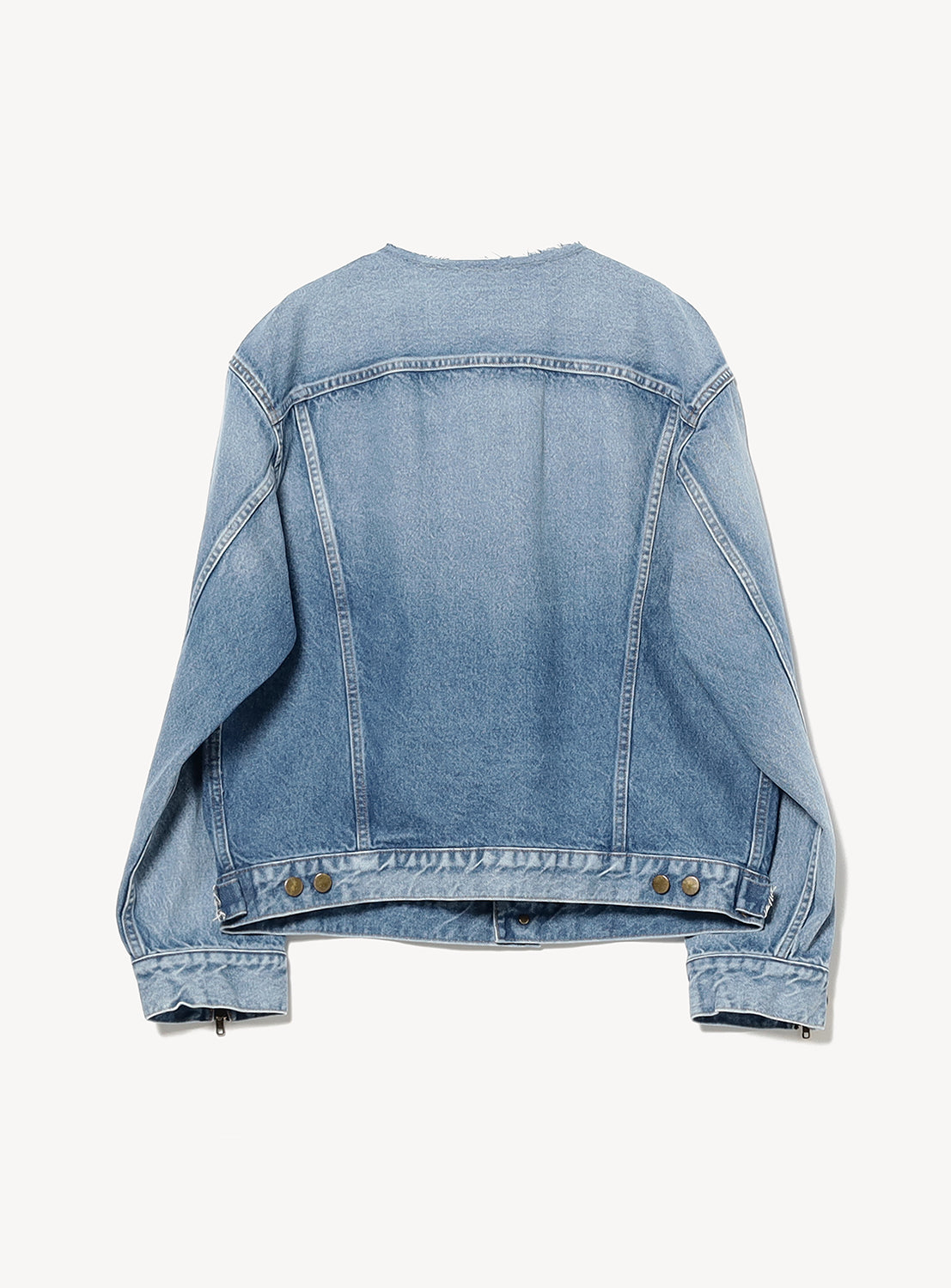 The INSCRIRE Used Collarless Denim Zip Jacket is shown laid flat with the back facing up, highlighting its seam detailing and metal buttons on the adjustable waistband. This light blue vintage wash jacket features long sleeves and is crafted from heavyweight cotton denim for lasting durability, set against a plain white background.