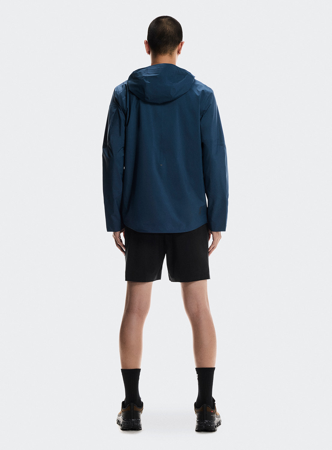 Back of model wearing a blue trek zip-up jacket with multiple zippers. and black shorts. 