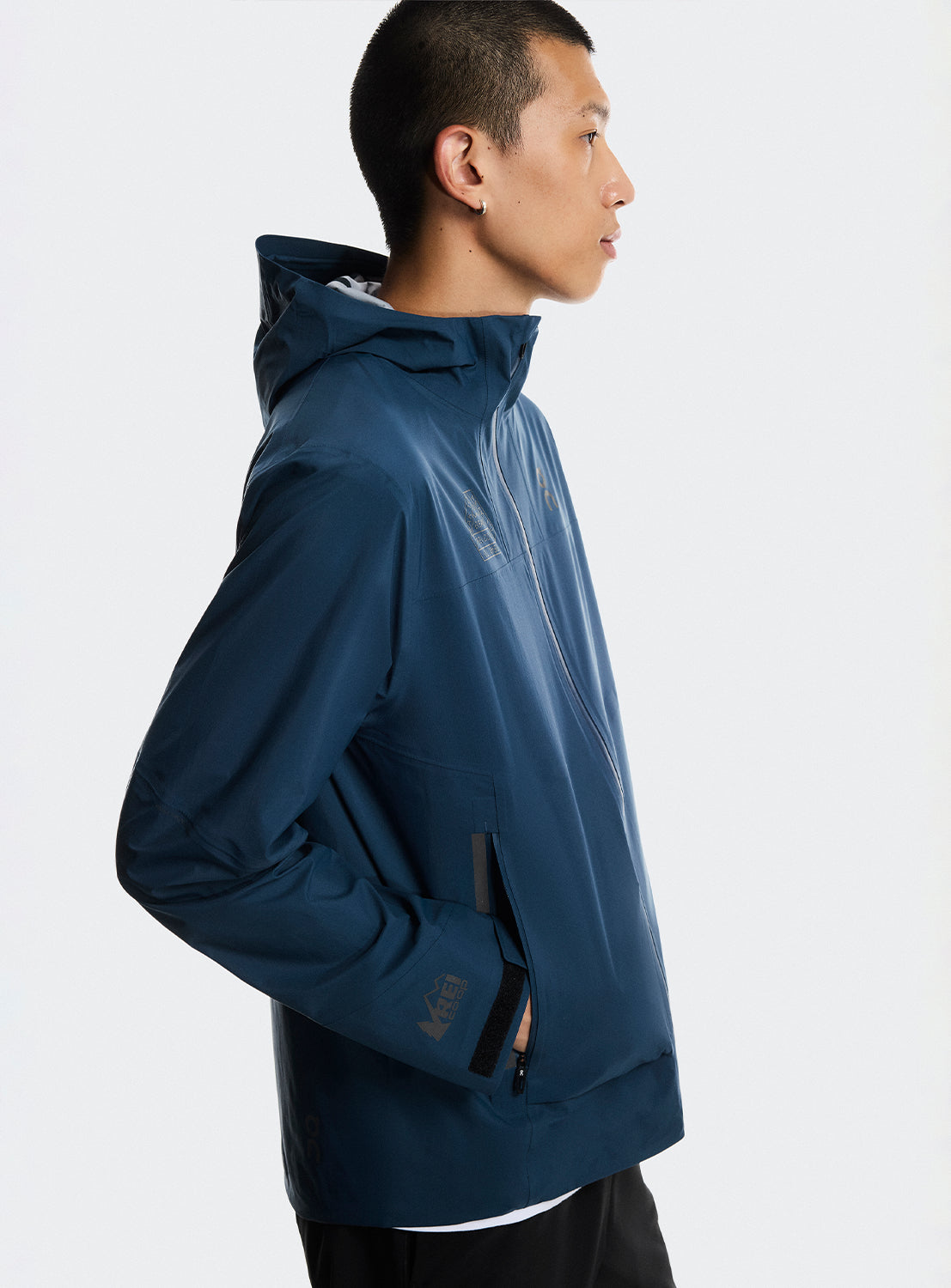 Side view of a model wearing a blue trek zip-up jacket with multiple zippers. 