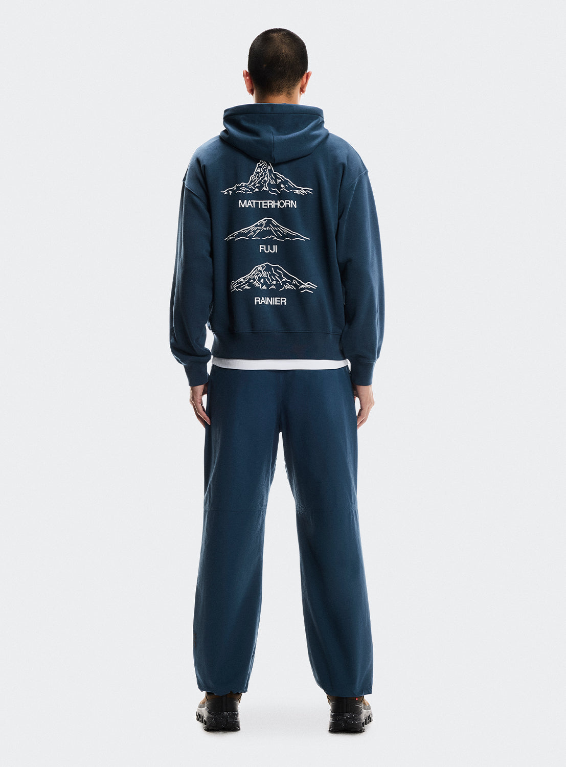 Person wearing a navy blue hoodie and pants with mountain designs graphics on the back. 