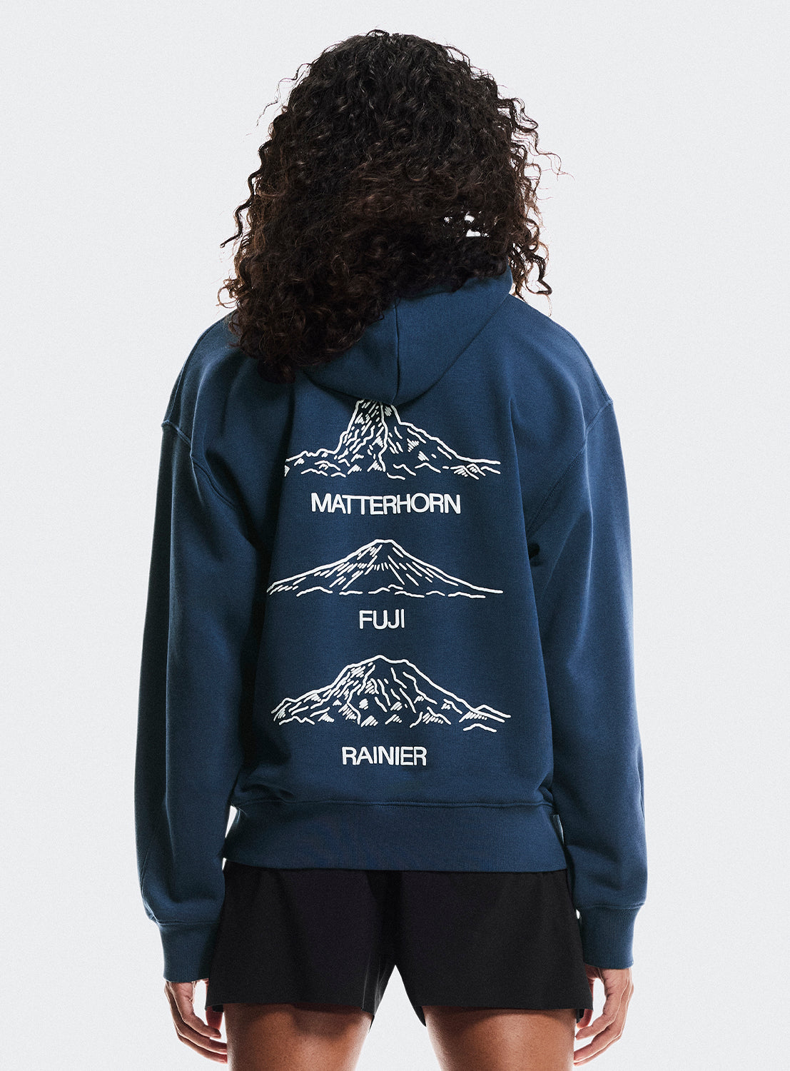 Model wearing navy blue hoodies with Matterhorn, Fuji, and Rainier mountain graphics. 
