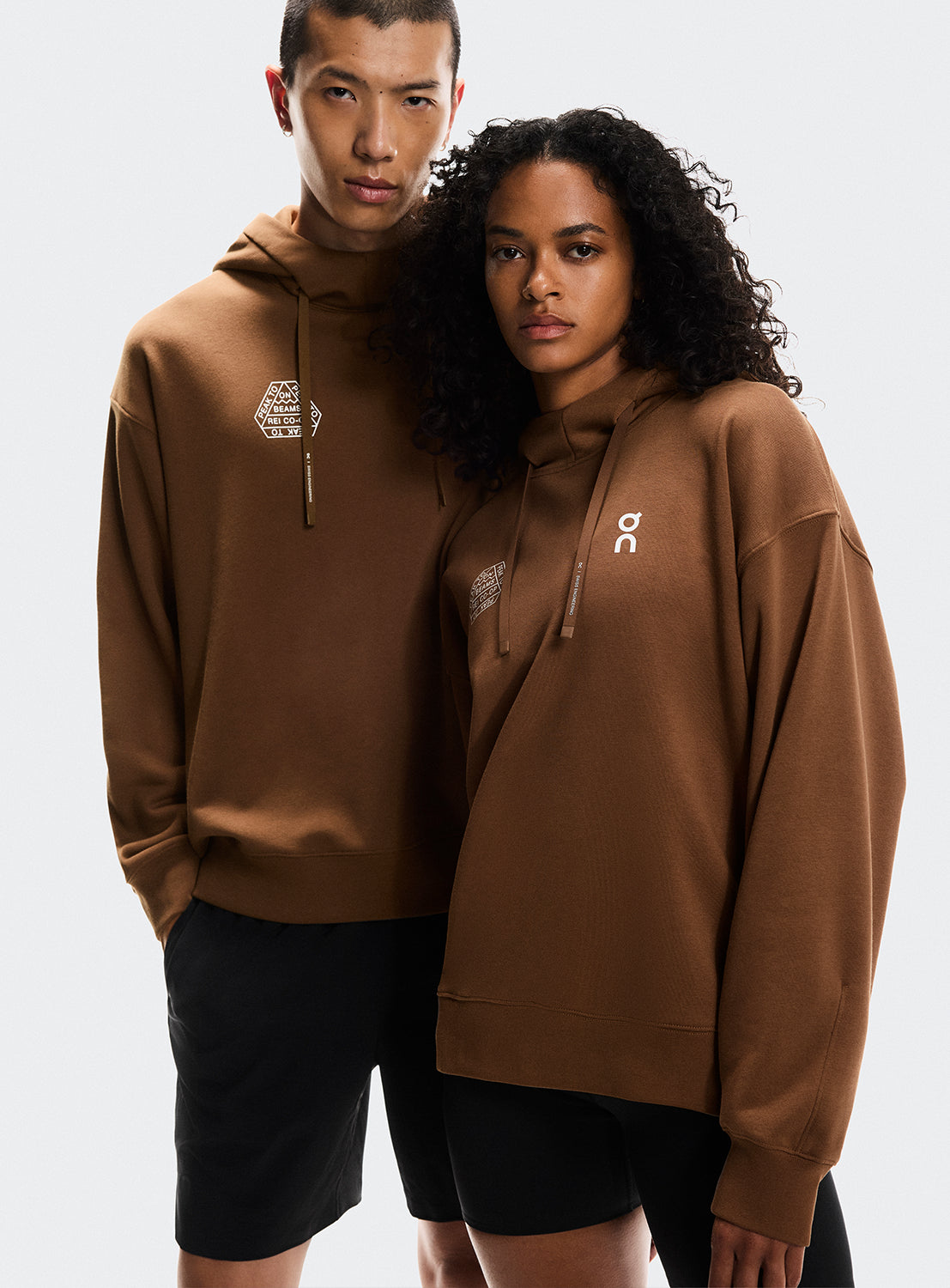 Models a wearing brown hoodies with On Running and BEAMS x REI CO-OP logo.