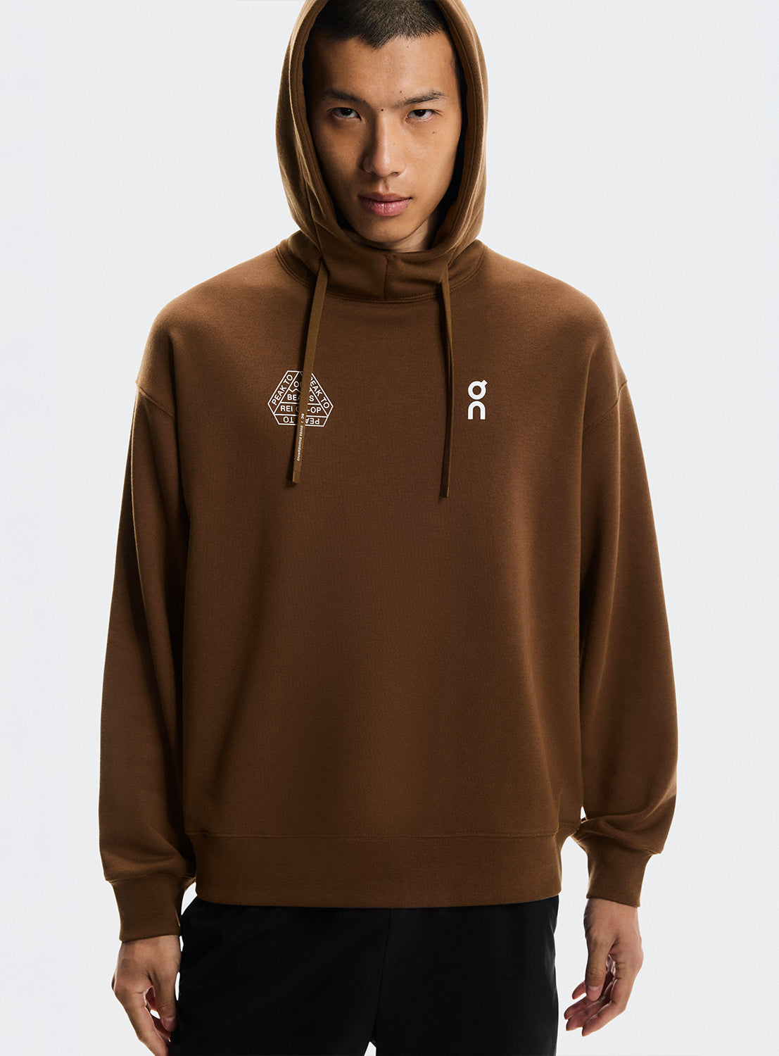 Model a wearing brown hoodies with On Running and BEAMS x REI CO-OP logo.