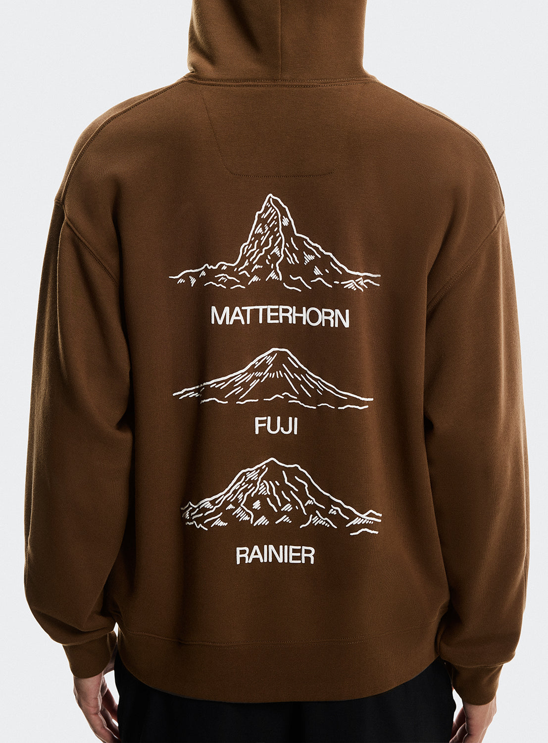 Model wearing a brown hoodie with Matterhorn, Mt. Fuji, and Mt Rainier on the back. 
