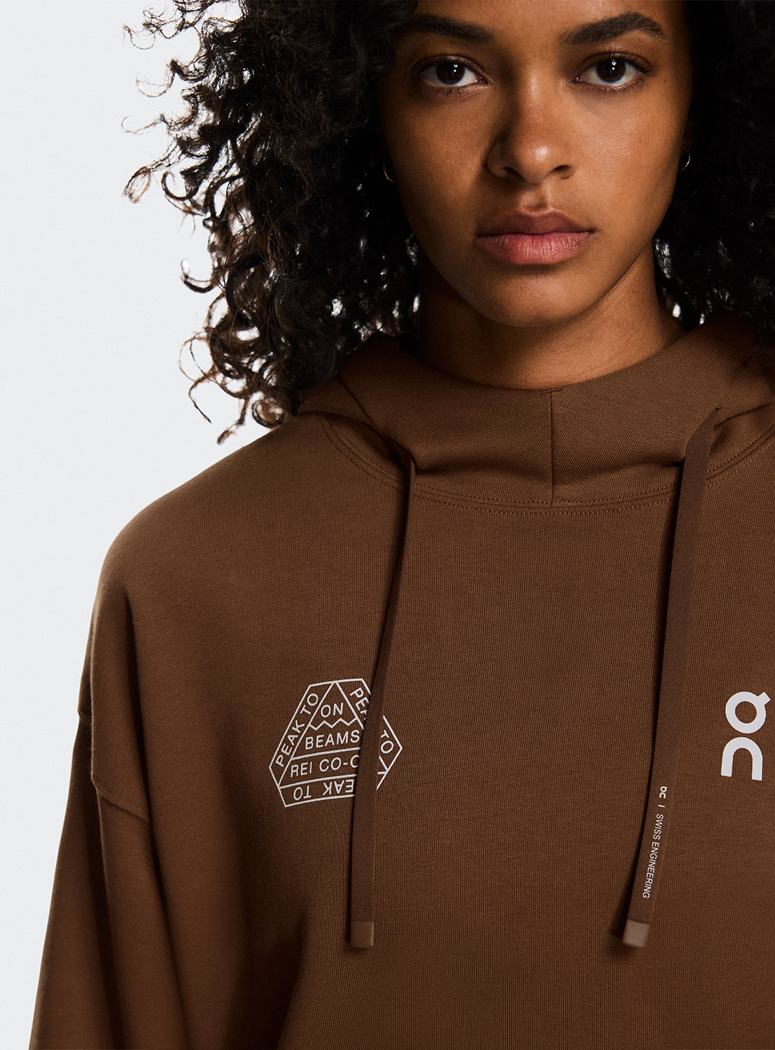 Model a wearing brown hoodies with On Running and BEAMS x REI CO-OP logo.