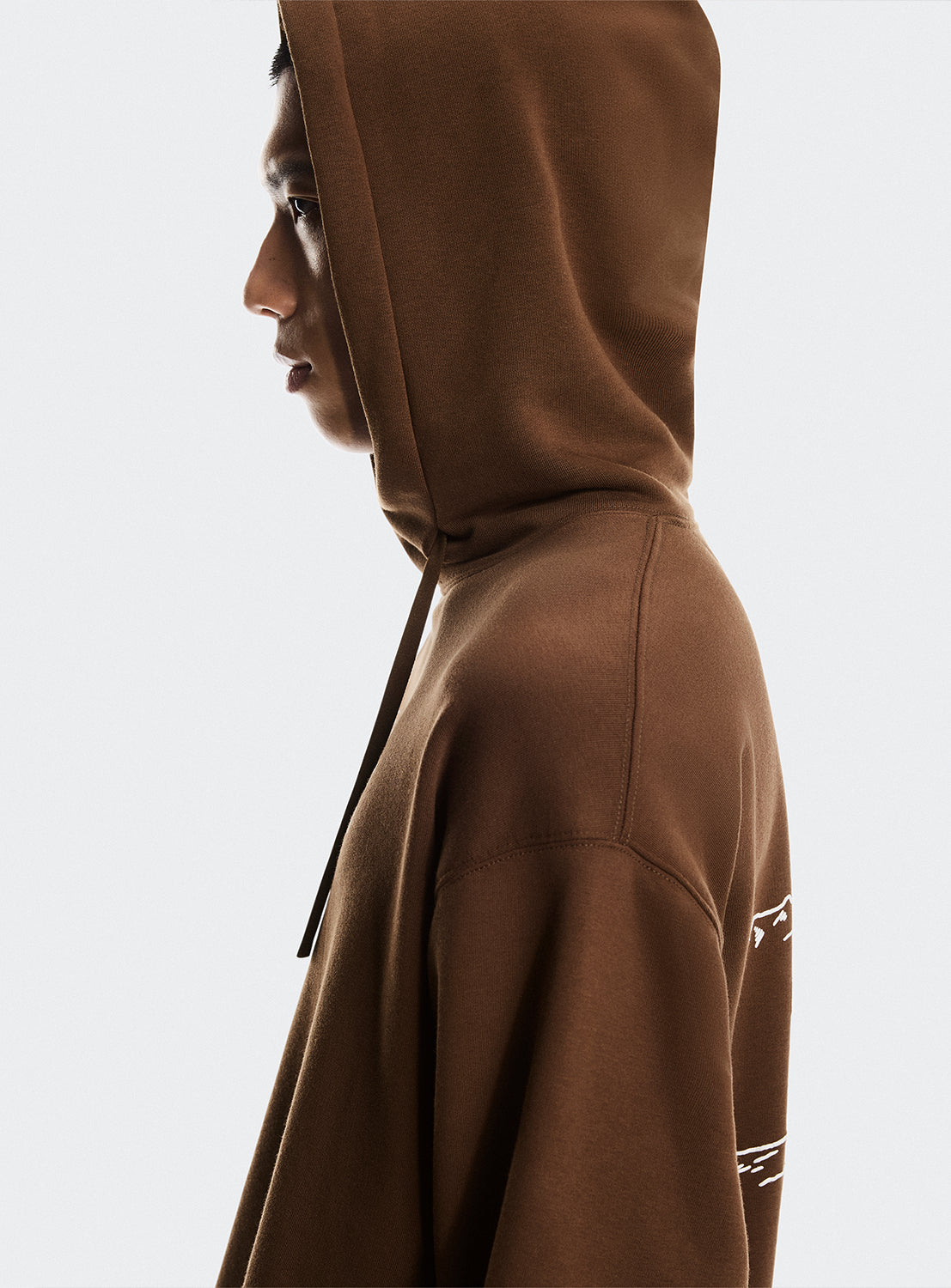 Model wearing a brown hoodie highlighting the hood detail. 