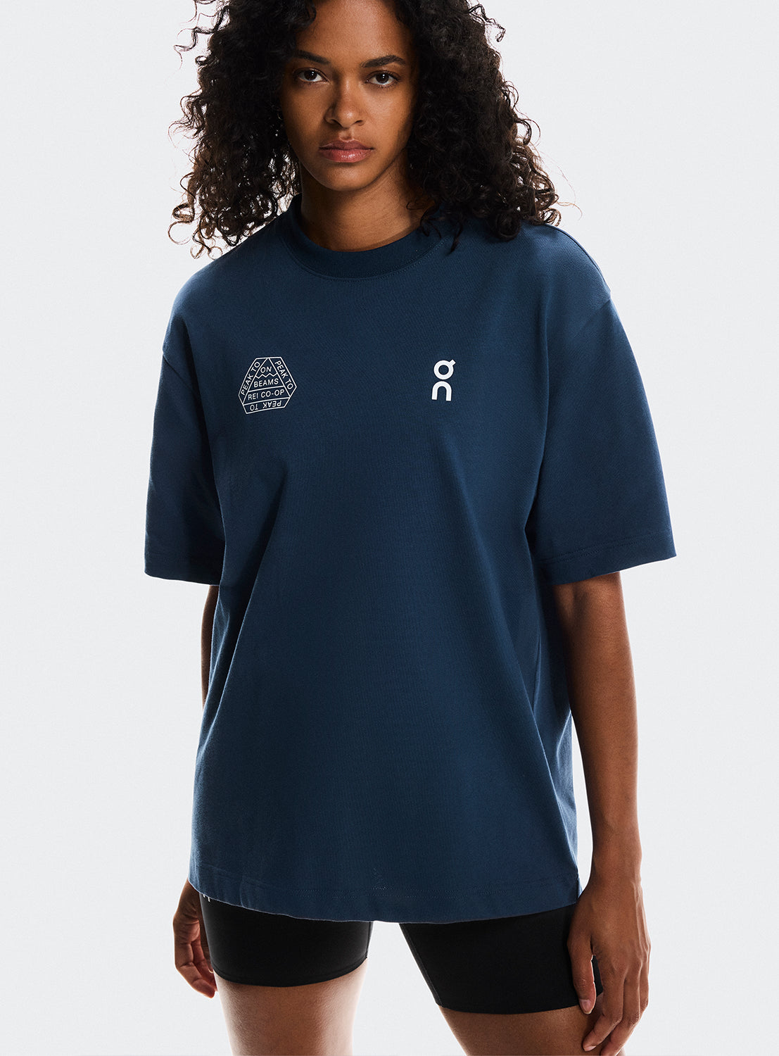 Model wearing navy blue t-shirt ON Running, BEAMS, and REI CO-OP logos. 