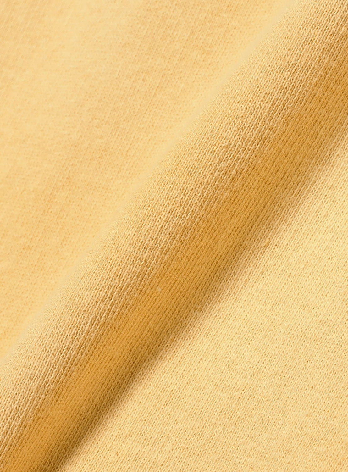 A close-up of the light yellow French terry fabric from the INSCRIRE Yellow Faded Zip Up Hoodie, highlighting its soft, textured surface and fine weave, with a gentle diagonal fold visible across the material.