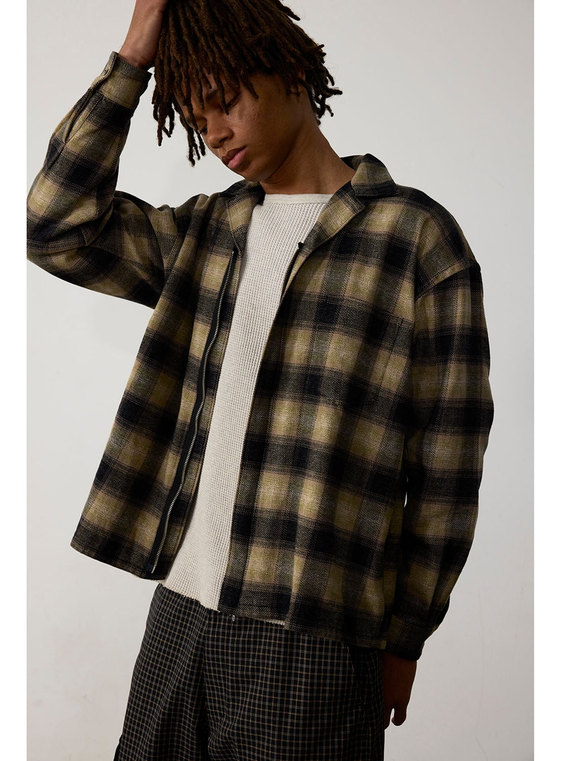 A person wearing a BEAMS Flannel Zip Open Collar Shirt in an olive and black check pattern over a cream-colored textured shirt.