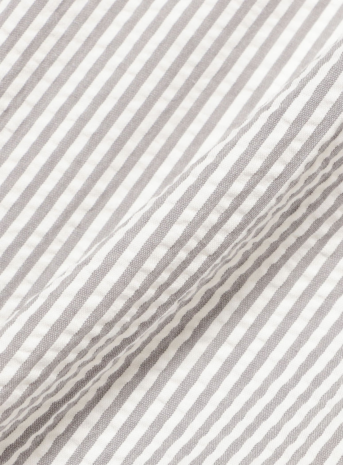 Close-up of white seersucker fabric with fine, diagonal gray stripes. The material is gently gathered, creating soft folds and shadows—ideal for crafting BEAMS BOY Relaxed Fit Seersucker Slacks that offer breezy comfort all summer long.