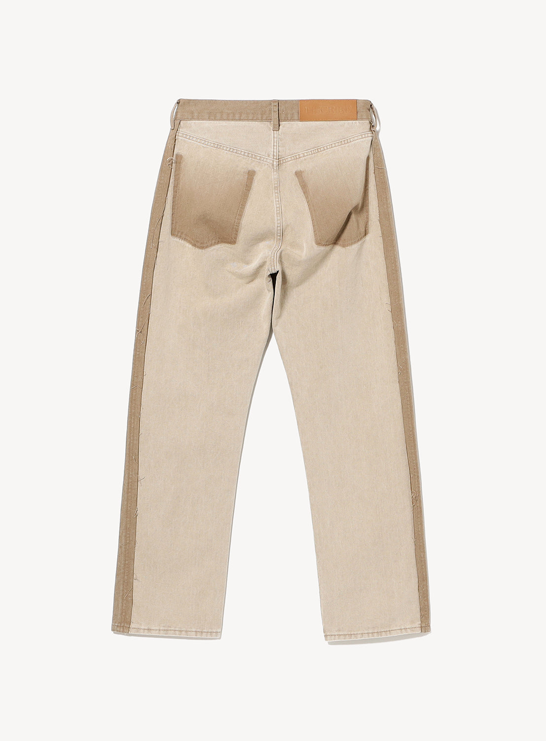 Back view of INSCRIRE's Colored Denim Straight-Leg Pants in beige, showcasing two oversized back pockets and contrasting tan side panels and waistband. Frayed edge detailing adds a distinctive touch, while a brown leather patch accents the right side of the waistband.