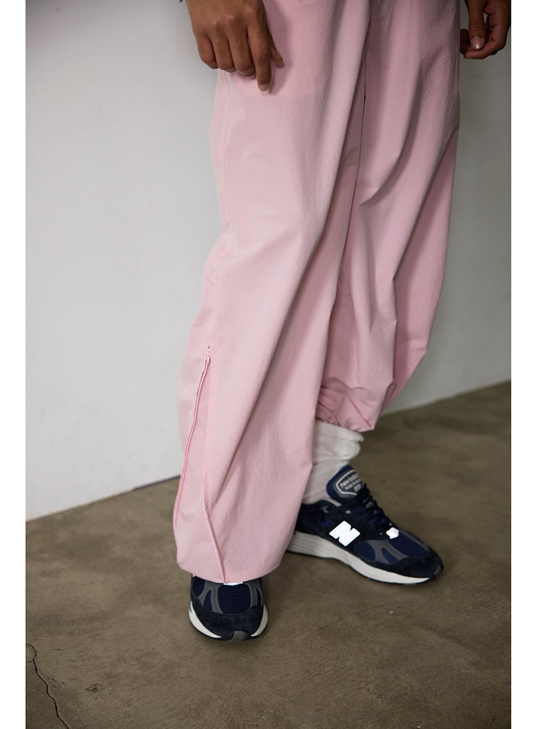 BEAMS Technical 2-Way Adjustable Easy Pants in light pink, featuring a wide-leg, water-repellent design with side zippers at the ankles, worn with dark blue sneakers and white socks.