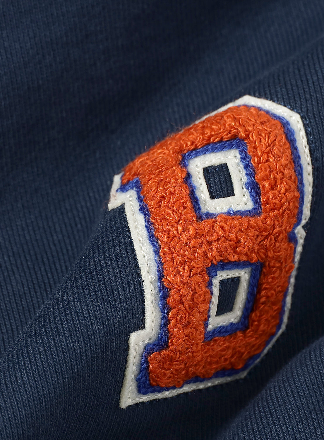 Close-up of an orange 'B' logo on a navy blue sweatpants. 