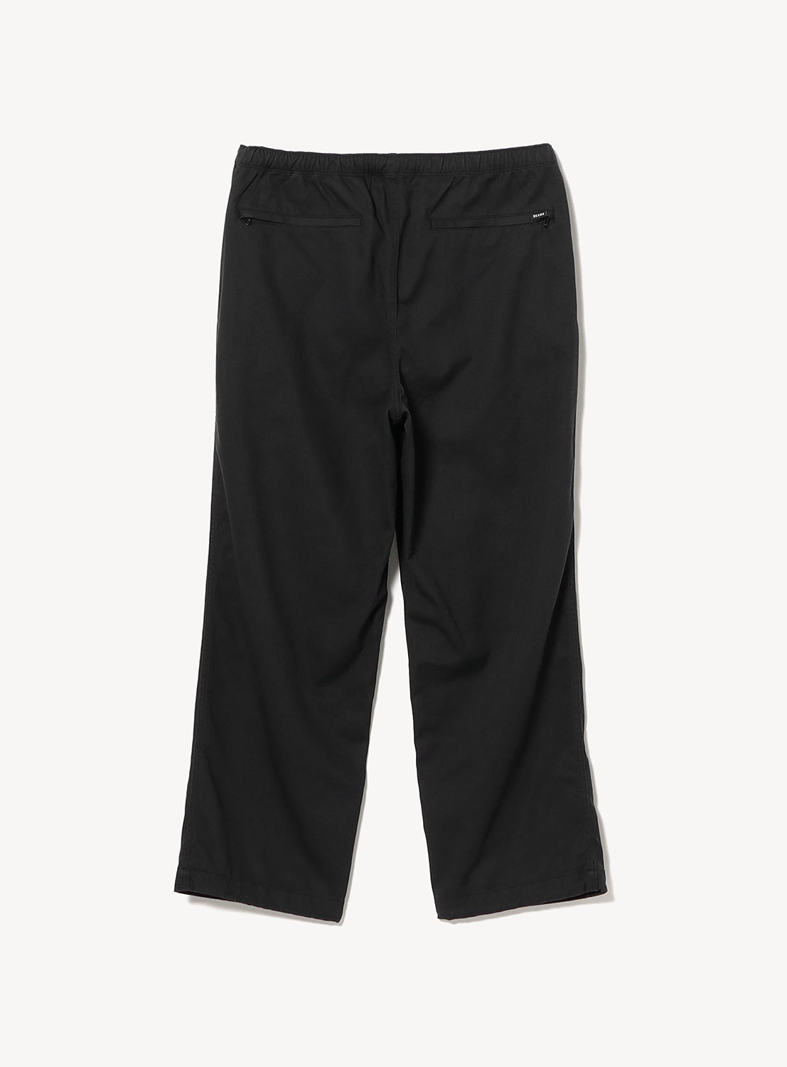 A pair of black Basic Twill Easy Pants from BEAMS, made from cotton twill with a straight-leg silhouette and elastic waistband, shown from the back on a white background. These relaxed-fit pants feature two zippered back pockets for added functionality.