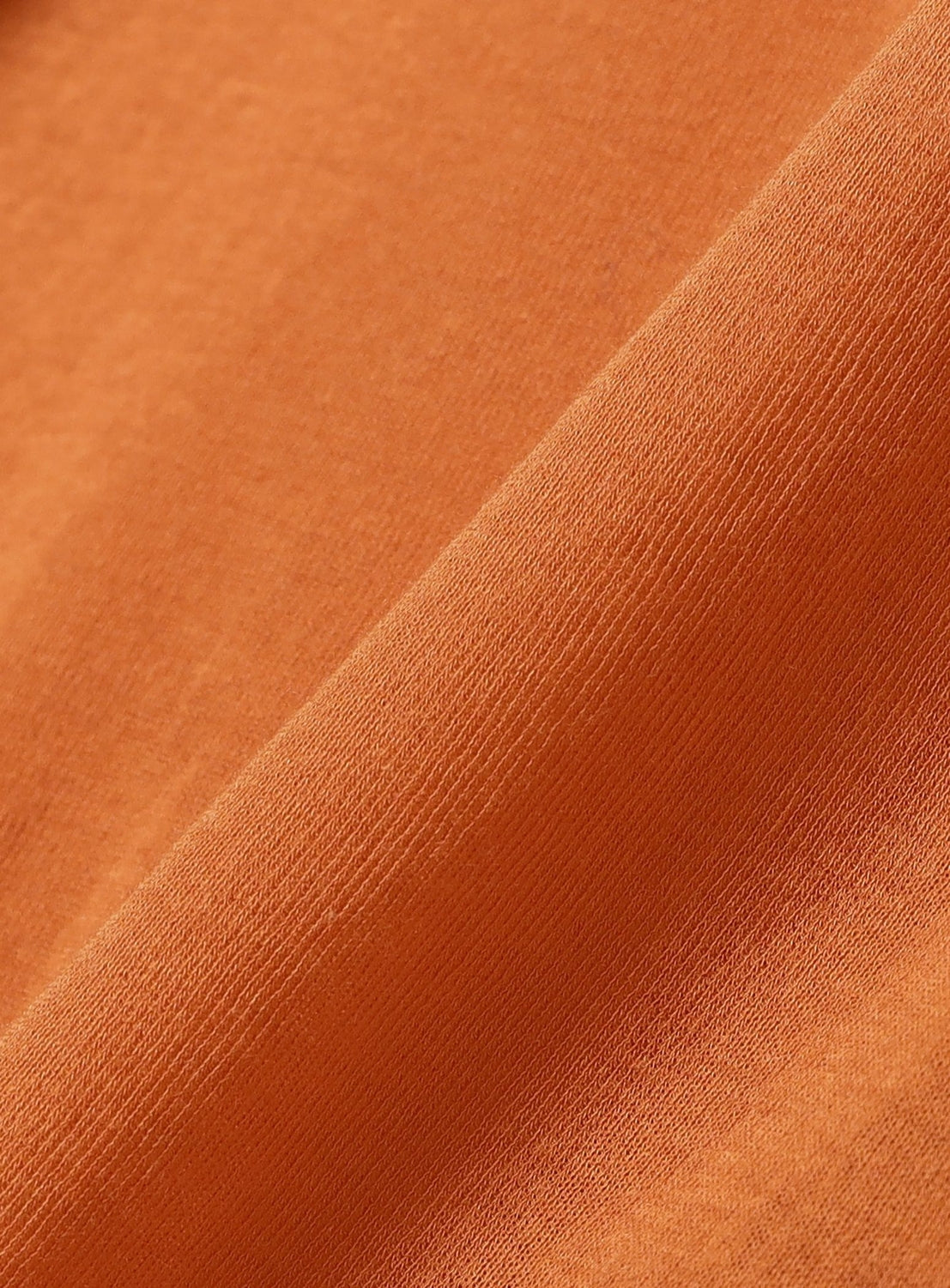 Close-up of an orange fabric with a soft, smooth texture and visible stitching detail, shown at an angle—highlighting the refined appeal and minimalist design of the Ernie Palo Sheer V-Neck Cardigan.