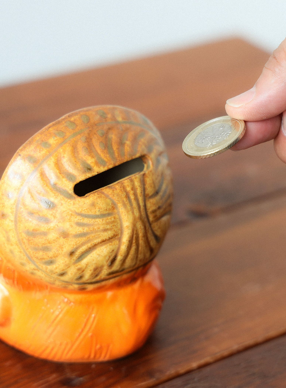 Person placing a coin into a decorative turtle-shaped money box on a wooden surface.