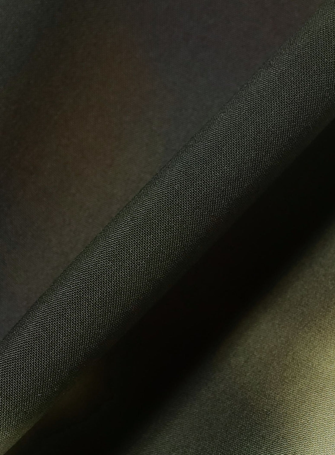 Close-up of folded dark green fabric with a fine, textured weave and soft shadows, showcasing the smooth surface and sturdy material—ideal for crafting the BAL Blur Pattern Open-Collar Short-Sleeve Shirt that highlights the brand’s original textile artwork.