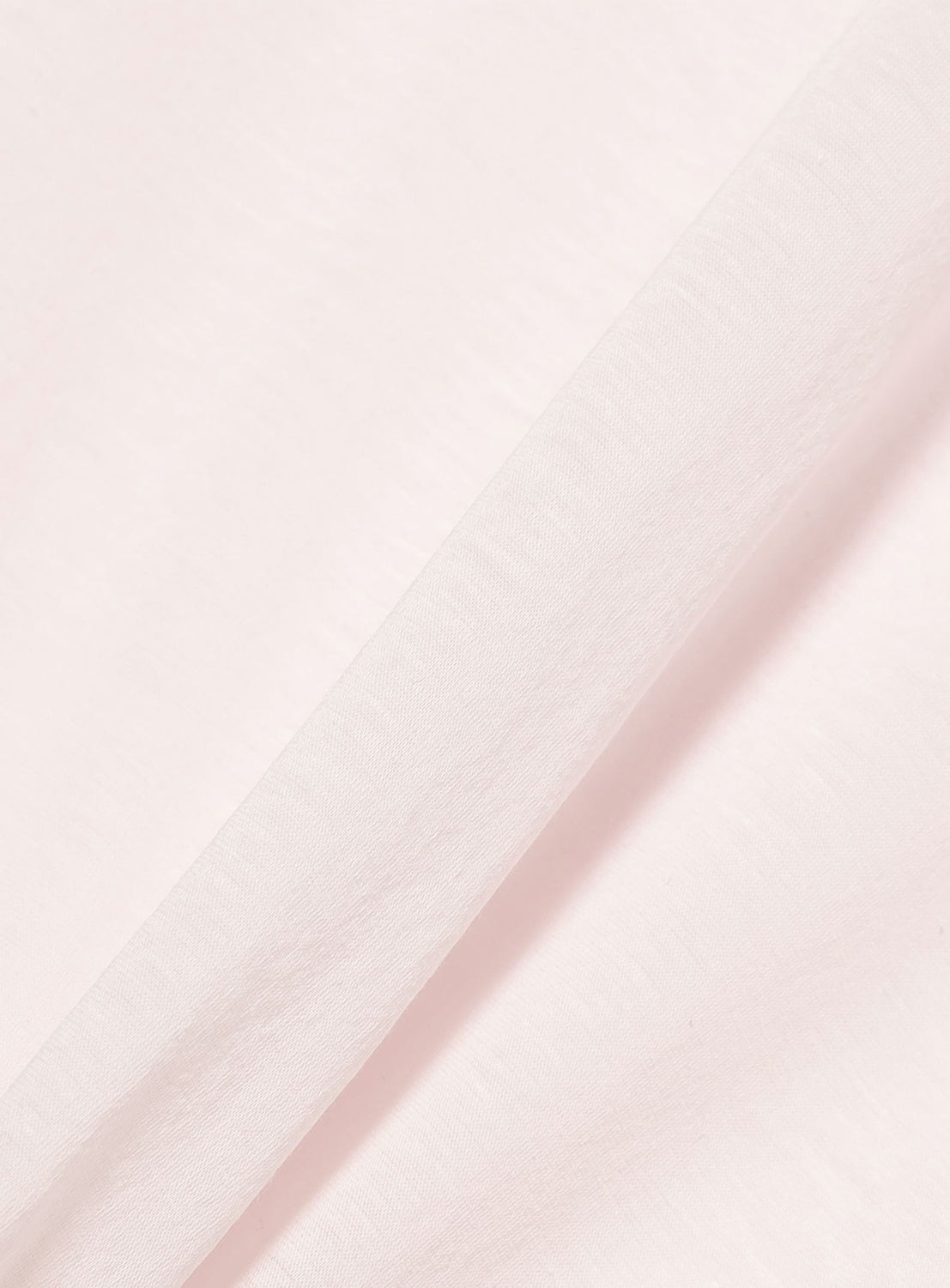 A close-up of the Ernie Palo Ringer T-shirt’s light pink cotton-nylon blend fabric, folded diagonally to highlight its smooth texture.