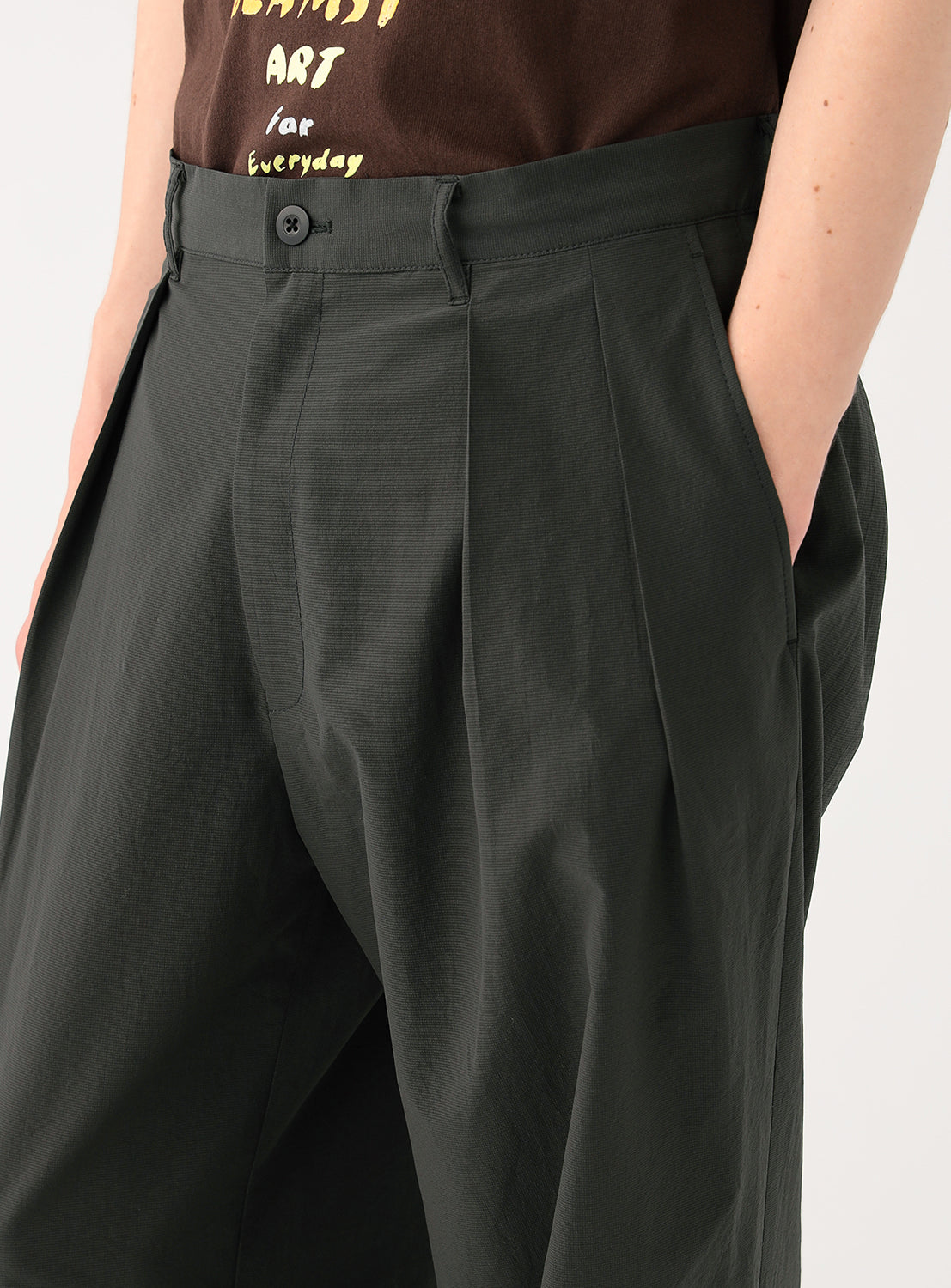 Close-up of a model's waist, highlighting the pleats and the fabric of the charcoal  pants.