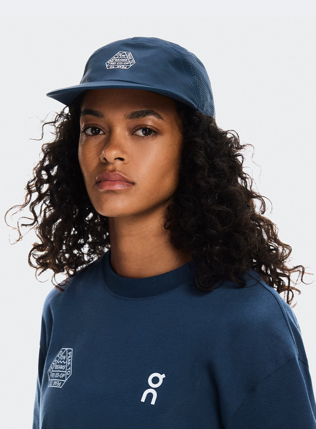 Model wearing a navy cap with adjustable strap and BEAMS X ON RUNNING X REI CO-OP logo.
