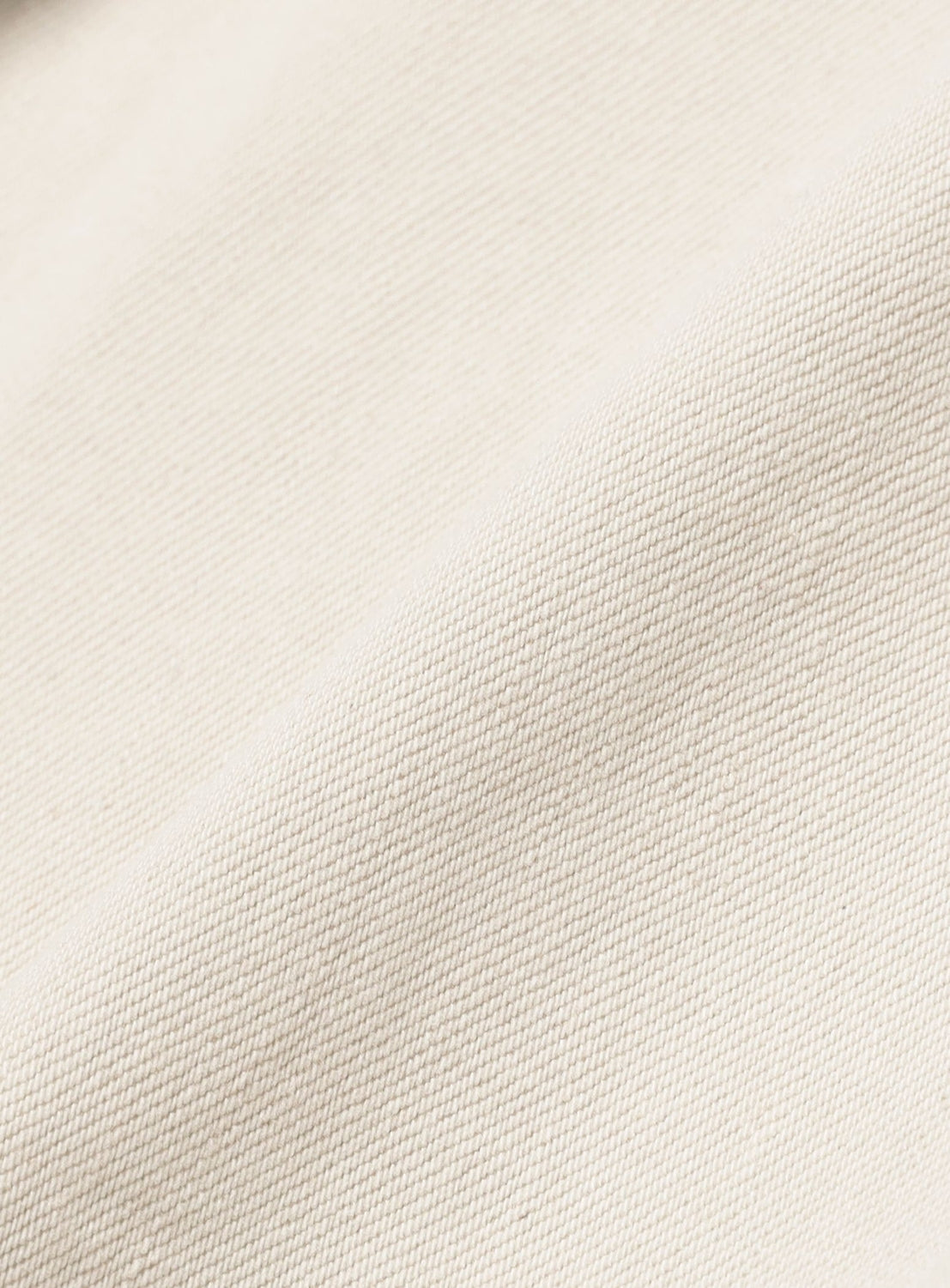 Close-up of the cream-colored fabric from SUGARHILL's Tattoo Flash Print Modern Denim Flared Cut, featuring a subtle diagonal weave and textured surface. Soft folds highlight the natural look, reminiscent of high-quality Okayama denim.