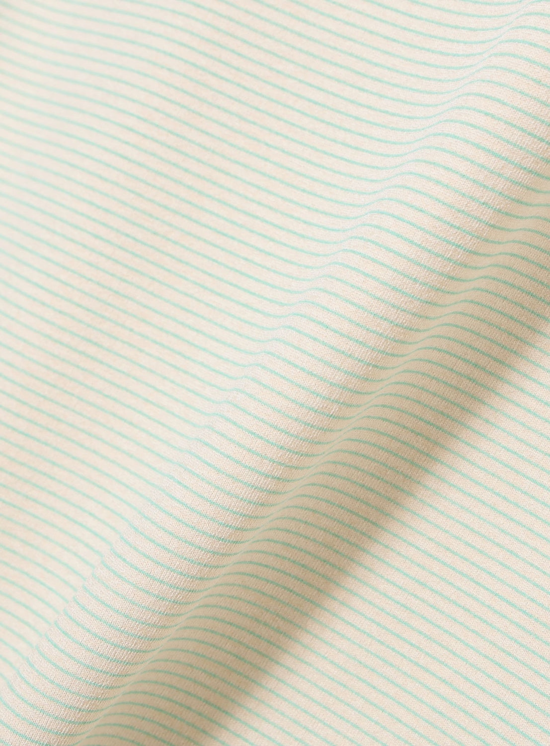 Close-up of the BEAMS Micro Stripe Wide Fit T-shirt’s cream-colored performance fabric, featuring thin, evenly spaced light green stripes and highlighting its gentle folds and soft, moisture-wicking texture.