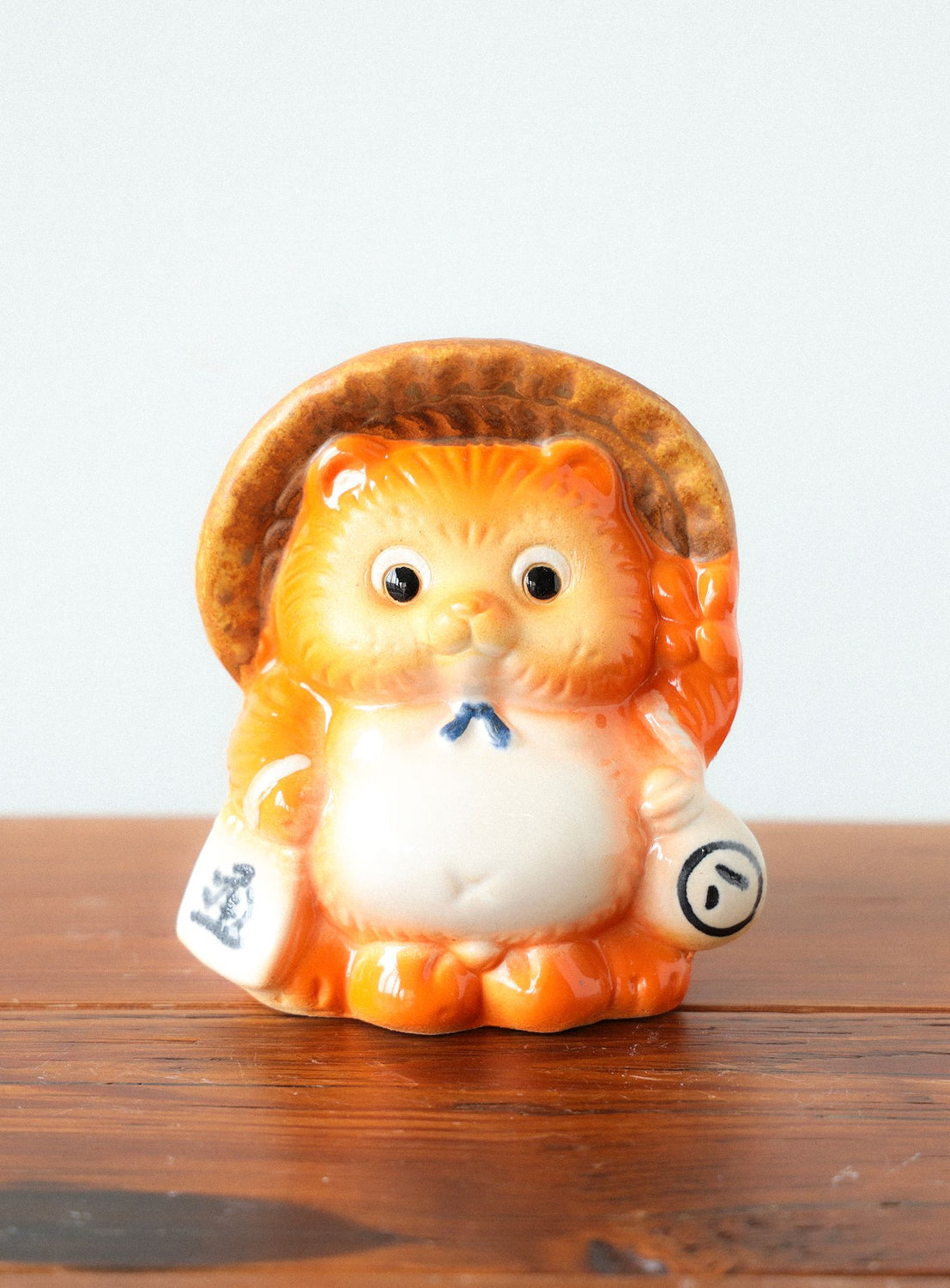 Ceramic cat figurine with a straw hat on a wooden surface