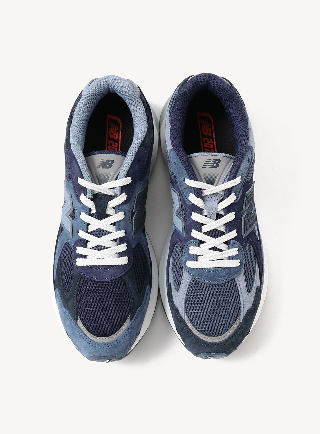 A pair of New Balance 2010 Exclusive Sneakers by BEAMS in blue and grey, displayed from above. The left shoe features white laces while the right has grey laces. Both are designed with black mesh and suede accents, red logo tags on the insoles, and are built on the classic NEW BALANCE 2010 silhouette with ABZORB cushioning for enhanced comfort.